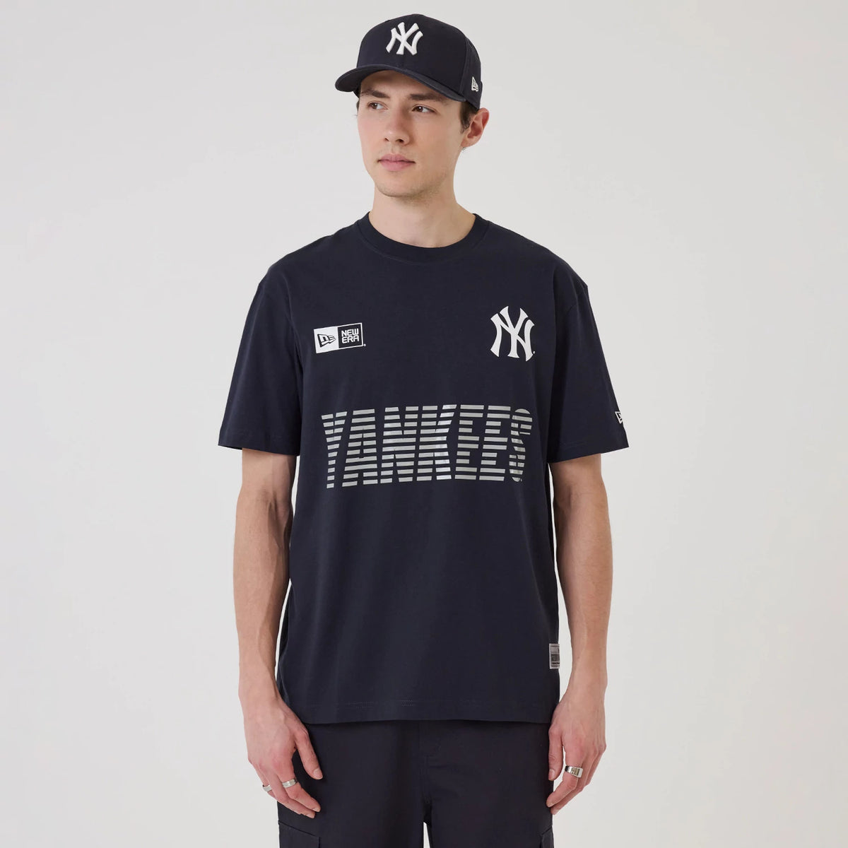 New Era New York Yankees MLB Match Navy T-Shirt, front view on-model showcasing the white embroidered Yankees logo on the chest, stacked lines forming YANKEES lettering in grey, and a small embroidered New Era logo near the shoulder.