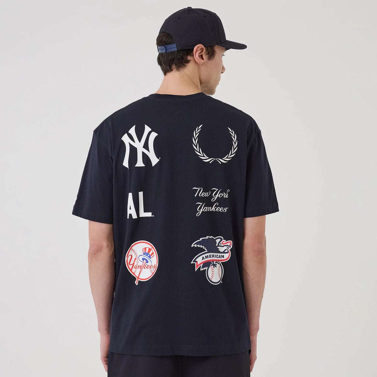 New Era New York Yankees MLB Match Navy T-Shirt, back view on-model showcasing multiple printed logos including the New York Yankees emblem, laurels, AL letters, and various team graphics in white and red against the navy fabric.