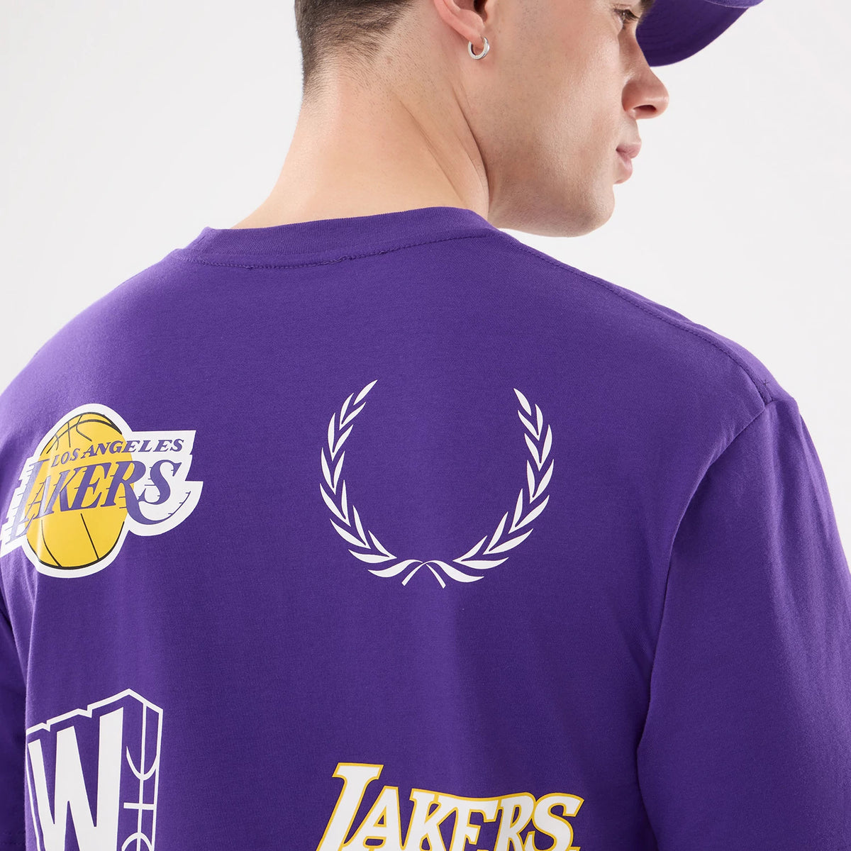 New Era LA Lakers NBA Match Purple T-Shirt, back view on a model showing the purple design with a series of printed graphics including the Los Angeles Lakers logo, a wreath emblem, and other team-related art across the upper back.
