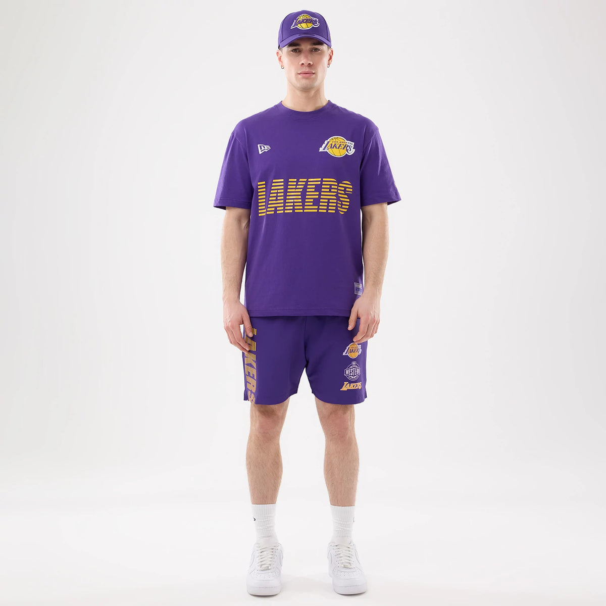 New Era LA Lakers NBA Match Purple T-Shirt, front view on-model with a matching purple cap and shorts, showing a yellow Lakers graphic across the chest, an embroidered New Era logo on the right shoulder, and the team logo on the left chest.