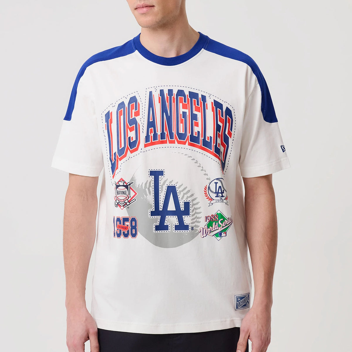 New Era LA Dodgers MLB Sport Classic White T-Shirt, front view on-model featuring large blue and red LOS ANGELES lettering, a prominent LA logo, various team patches across the chest, and blue panels on the shoulders and collar.