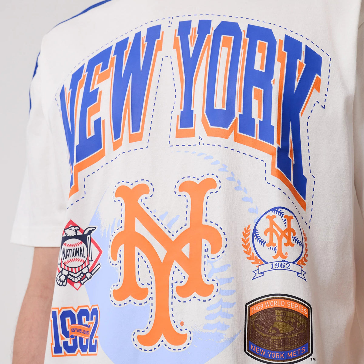New Era New York Mets MLB Sport Classic White T-Shirt, front view showcasing blue and orange New York lettering with additional Mets logos and a commemorative patch, creating an eye-catching graphic design across the chest.