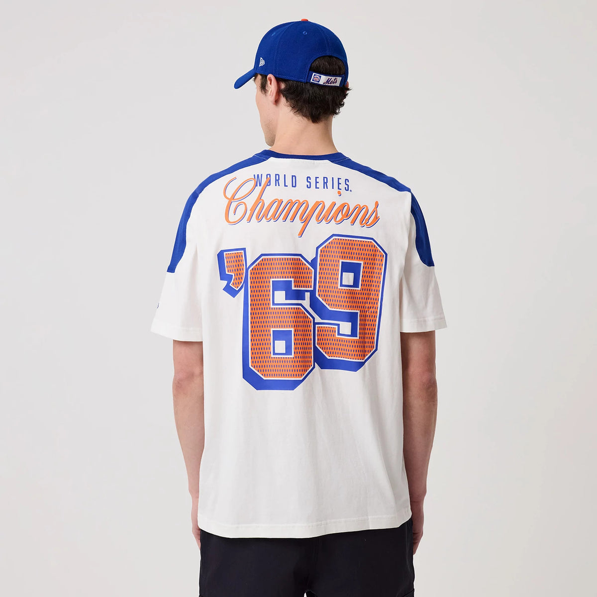New Era New York Mets MLB Sport Classic White T-Shirt, back view on a model in a matching blue cap, showing orange lettering World Series Champions and a large blue and orange '69 across the back.