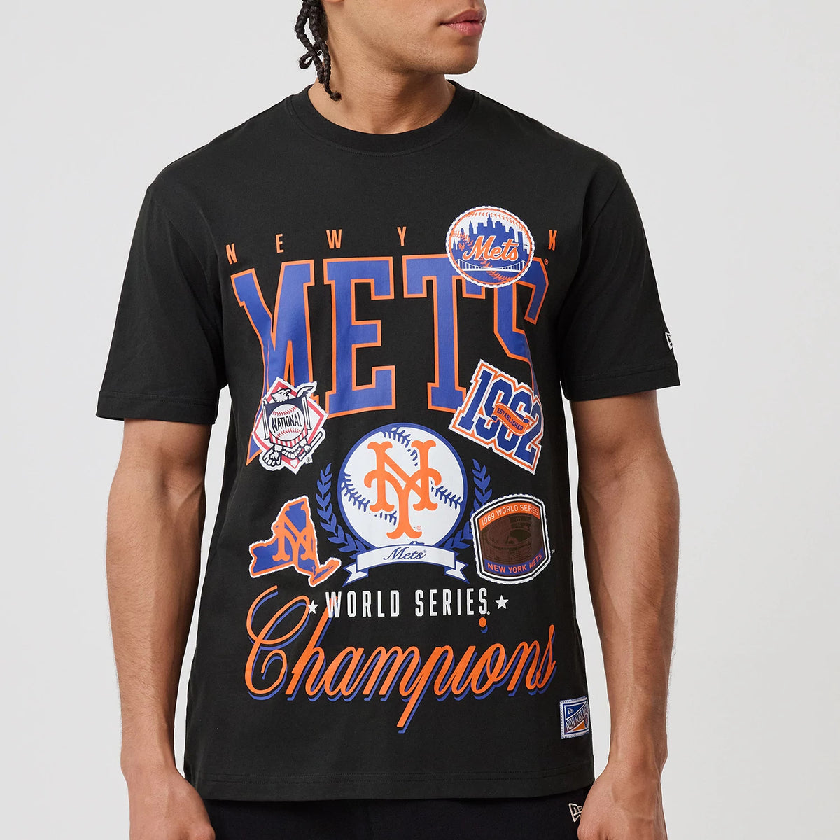 New Era New York Mets MLB Sport Classic Black T-Shirt, front view on-model showing METS lettering with orange and blue graphics and patches, including the team's logo and championship badges, and a printed New Era logo on the sleeve.