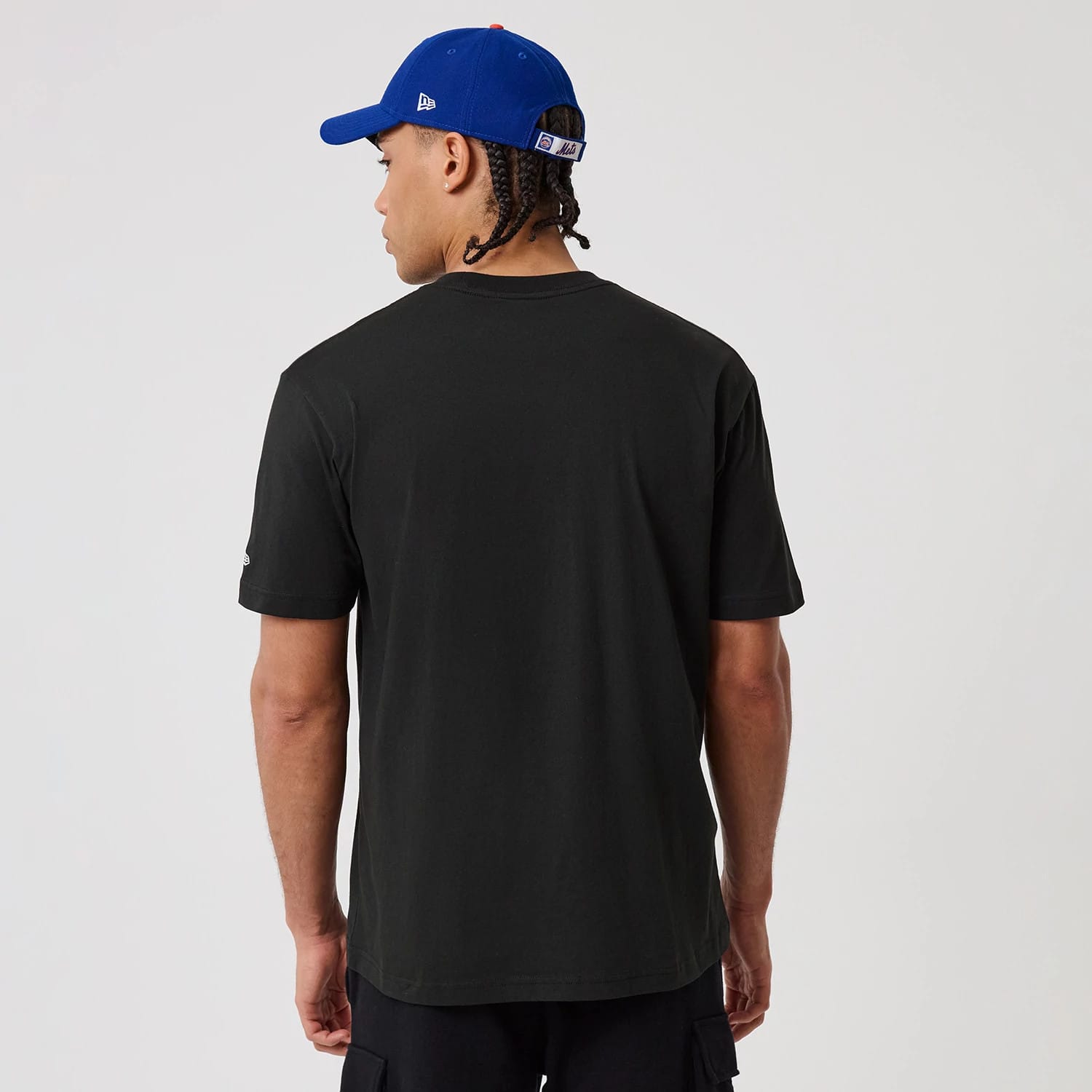 New Era New York Mets MLB Sport Classic Black T-Shirt, back view on-model displaying the plain back of the black t-shirt with short sleeves, styled simply with a blue cap showing a white embroidered New Era logo on the side.