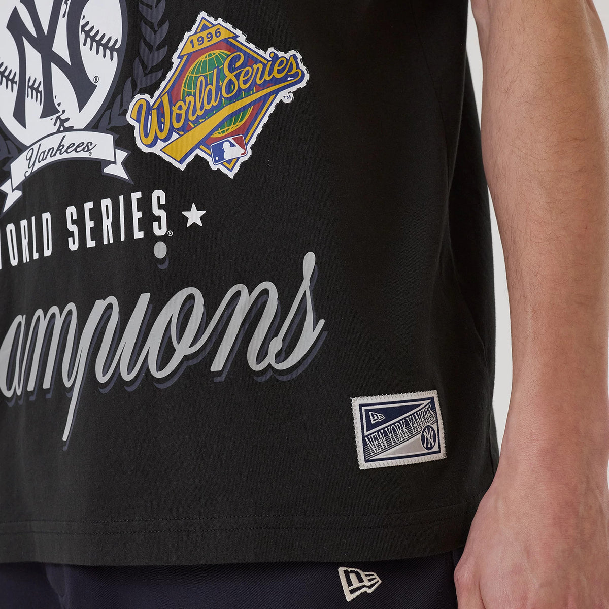 New Era New York Yankees MLB Sport Classic Black T-Shirt, front view showing World Series graphics and Champions lettering across the chest, with a woven New Era patch at the lower hem and a matching cap logo on the shorts.