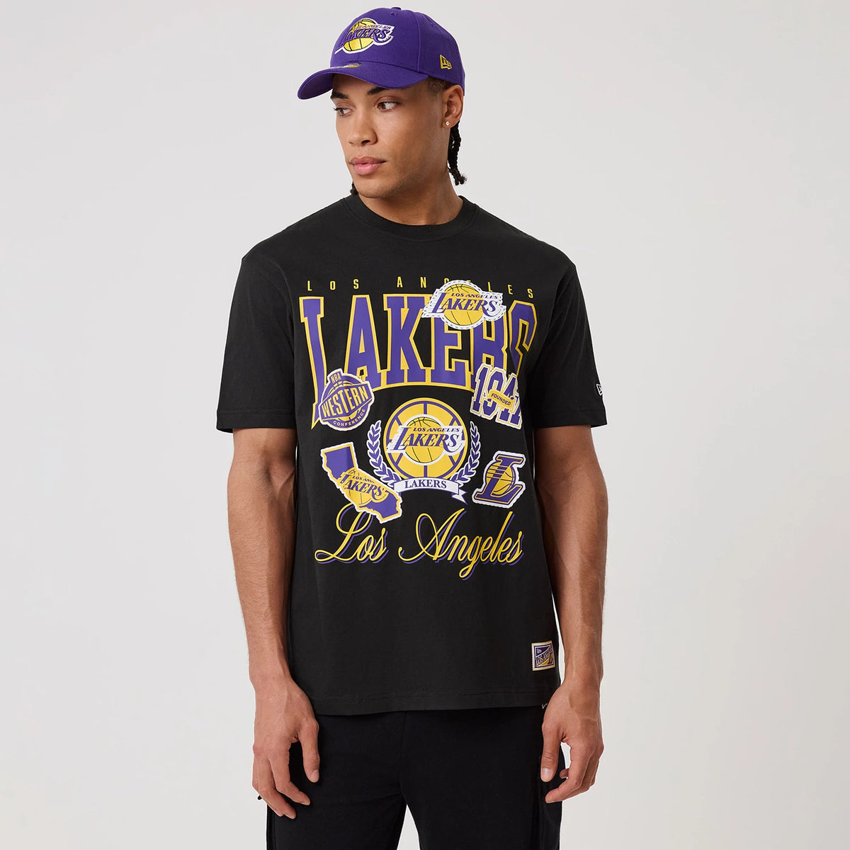 New Era LA Lakers NBA Sport Classic Black T-Shirt, front view on-model showing Lakers and Los Angeles lettering in purple and gold, multiple Lakers logos across the chest and an embroidered New Era logo on the left sleeve.