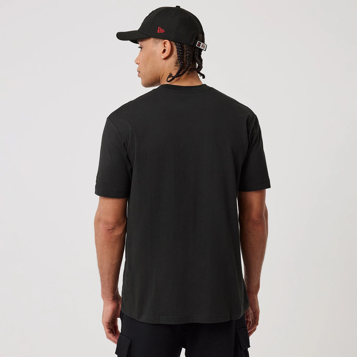 New Era Chicago Bulls NBA Sport Classic Black T-Shirt, back view on a model showing the plain black back of the shirt with a matching black cap featuring a red embroidered New Era logo on the side and a snapback closure.