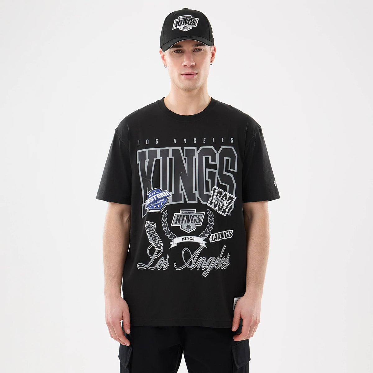New Era LA Kings NHL Sport Classic Black T-Shirt, front view on-model showing large grey Kings lettering across the chest with various team logos and Los Angeles script below, paired with a matching black cap featuring an embroidered team logo.