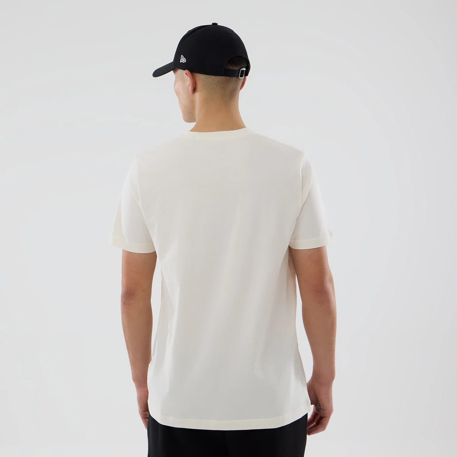 New Era Grapefruit League Logo MLB Spring Training 2026 Cream T-Shirt, back view on-model showing the plain cream back without graphics or logos, styled with a black cap that has a raised New Era logo on the side.