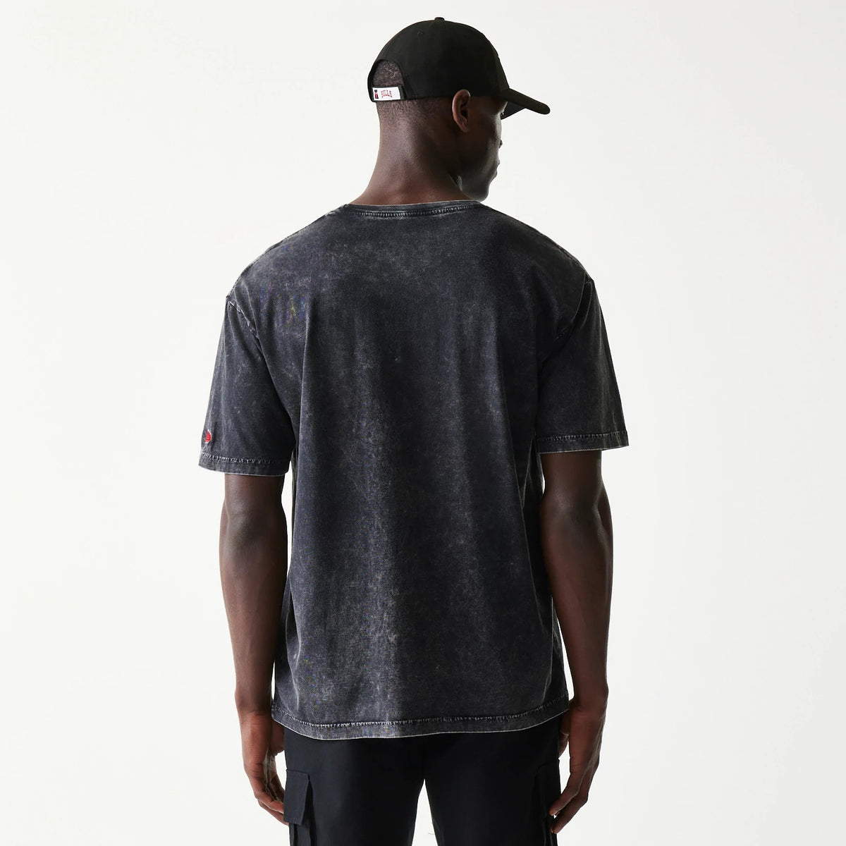New Era Chicago Bulls NBA Black T-Shirt, rear view on-model showing a washed black finish with a small red embroidered Bulls logo on the sleeve, paired with black trousers and a black cap.