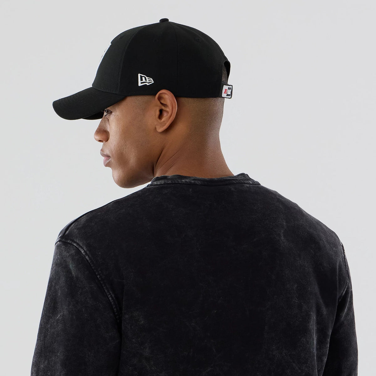 New Era Las Vegas Raiders NFL Laurel Wreath Black Crew Neck Sweater, rear view on a model wearing a black curved-visor cap featuring the New Era flag logo on the left side and the black textured sweater with a relaxed fit.