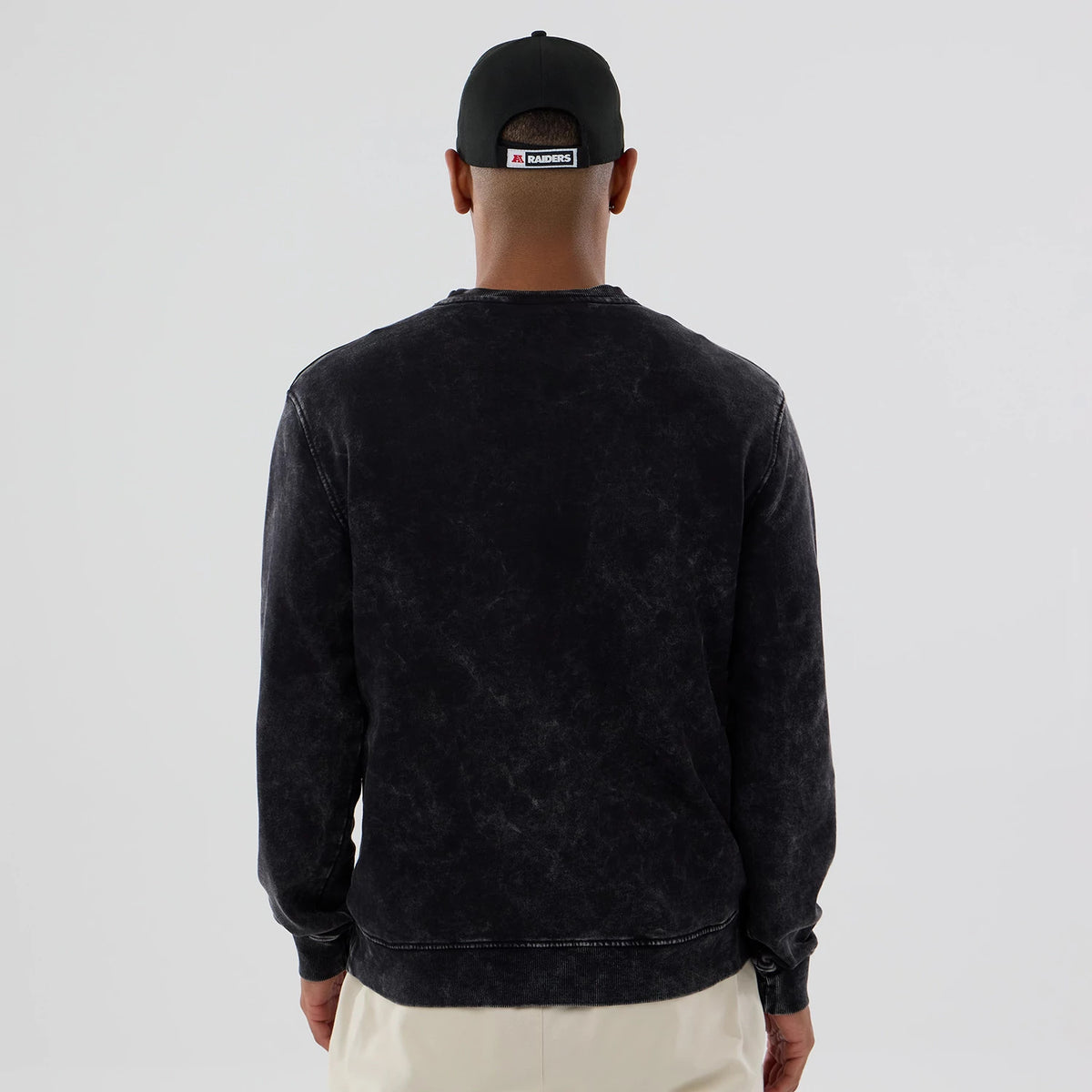 New Era Las Vegas Raiders NFL Laurel Wreath Black Crew Neck Sweater, back view on a model showing the vintage wash effect on the black fabric with ribbed cuffs and hem for a casual look.