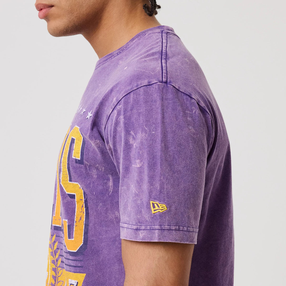 New Era LA Lakers NBA Purple T-Shirt, side view showing the faded purple fabric with LA Lakers lettering in yellow across the chest, a small yellow embroidered New Era logo on the sleeve, and seam on the shoulder.