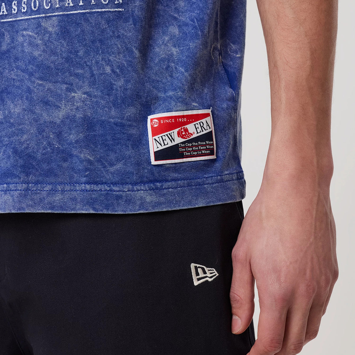 New Era Oklahoma City Thunder NBA Blue T-Shirt, front view showing a New Era patch near the hem on a mottled blue fabric, paired with dark trousers that feature an embroidered New Era logo near the pocket.