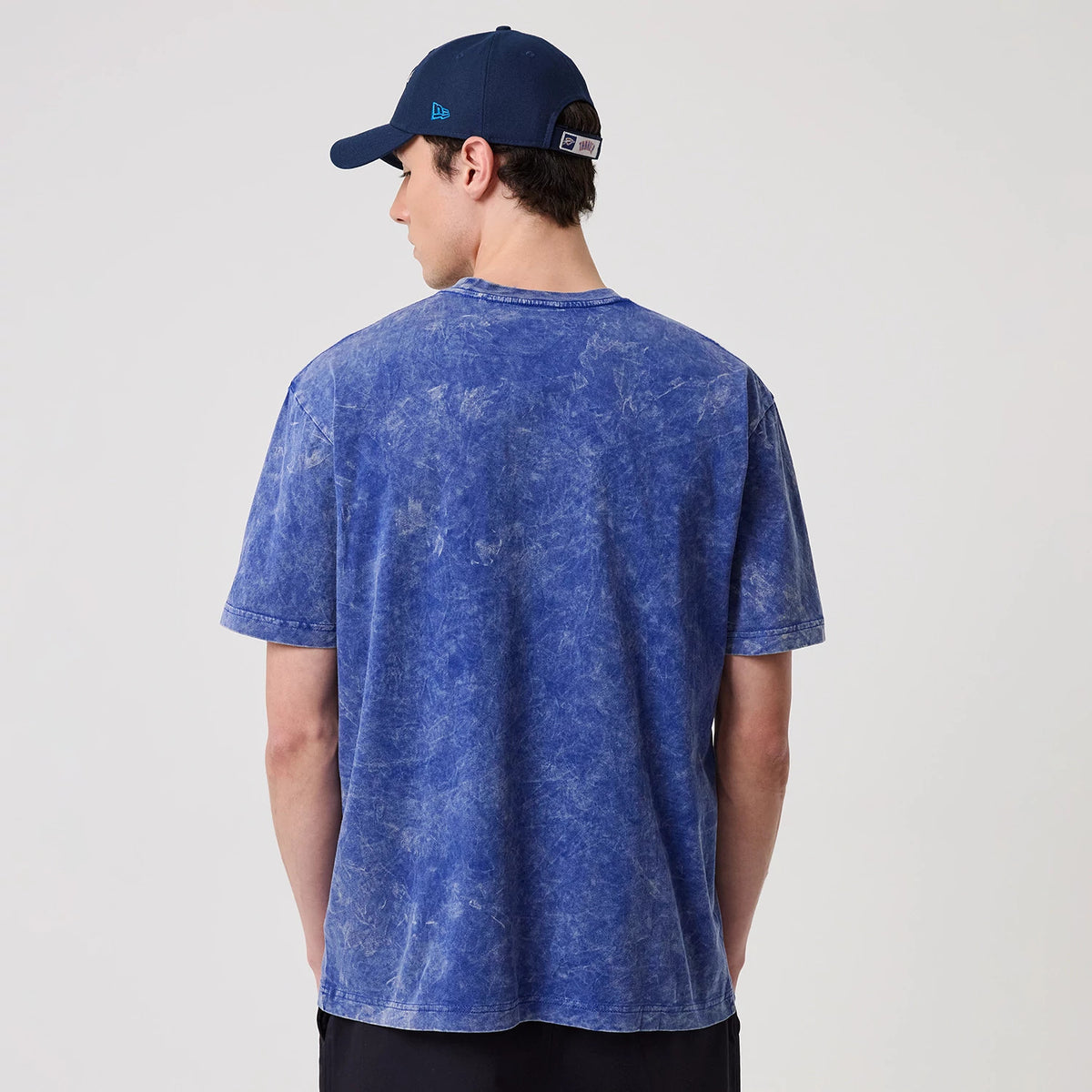 New Era Oklahoma City Thunder NBA Blue T-Shirt, back view on-model showing the mottled blue fabric with short sleeves, paired with a blue cap featuring an embroidered New Era logo on the side.