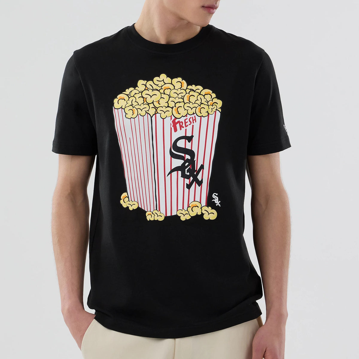 New Era Chicago White Sox MLB Popcorn Black T-Shirt, front view on a model, featuring a large printed graphic of a red and white popcorn box with yellow popcorn overflowing, showcasing the Sox logo prominently on the box.