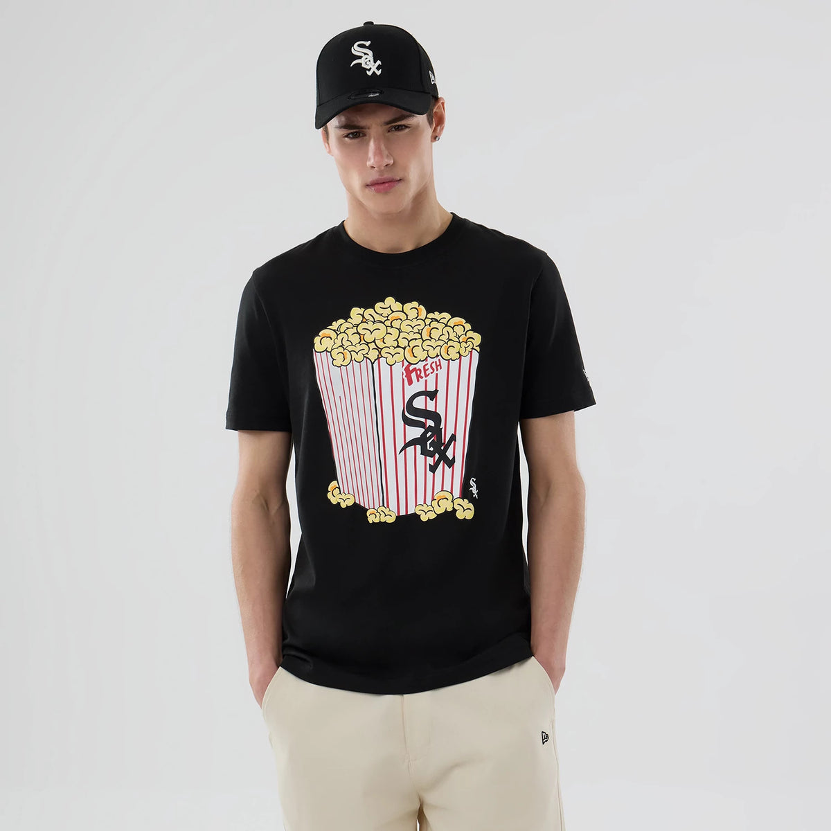 New Era Chicago White Sox MLB Popcorn Black T-Shirt, front view showing a graphic of a popcorn box overflowing with popcorn, featuring the team logo front and centre, on a model styled with a matching black cap.