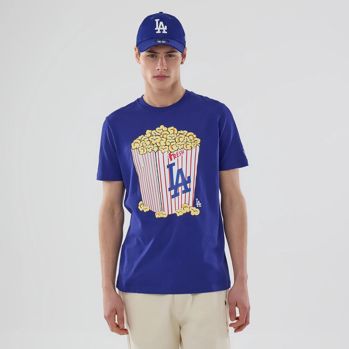New Era LA Dodgers MLB Popcorn Dark Blue T-Shirt, front view on-model featuring a popcorn box graphic with LA lettering on the chest and a small embroidered LA Dodgers logo near the hem.