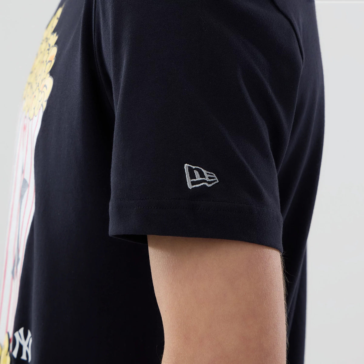 New Era New York Yankees MLB Popcorn Navy T-Shirt, side view showing a white embroidered New Era logo on the sleeve, with a glimpse of a popcorn graphic on the front against the dark navy fabric.