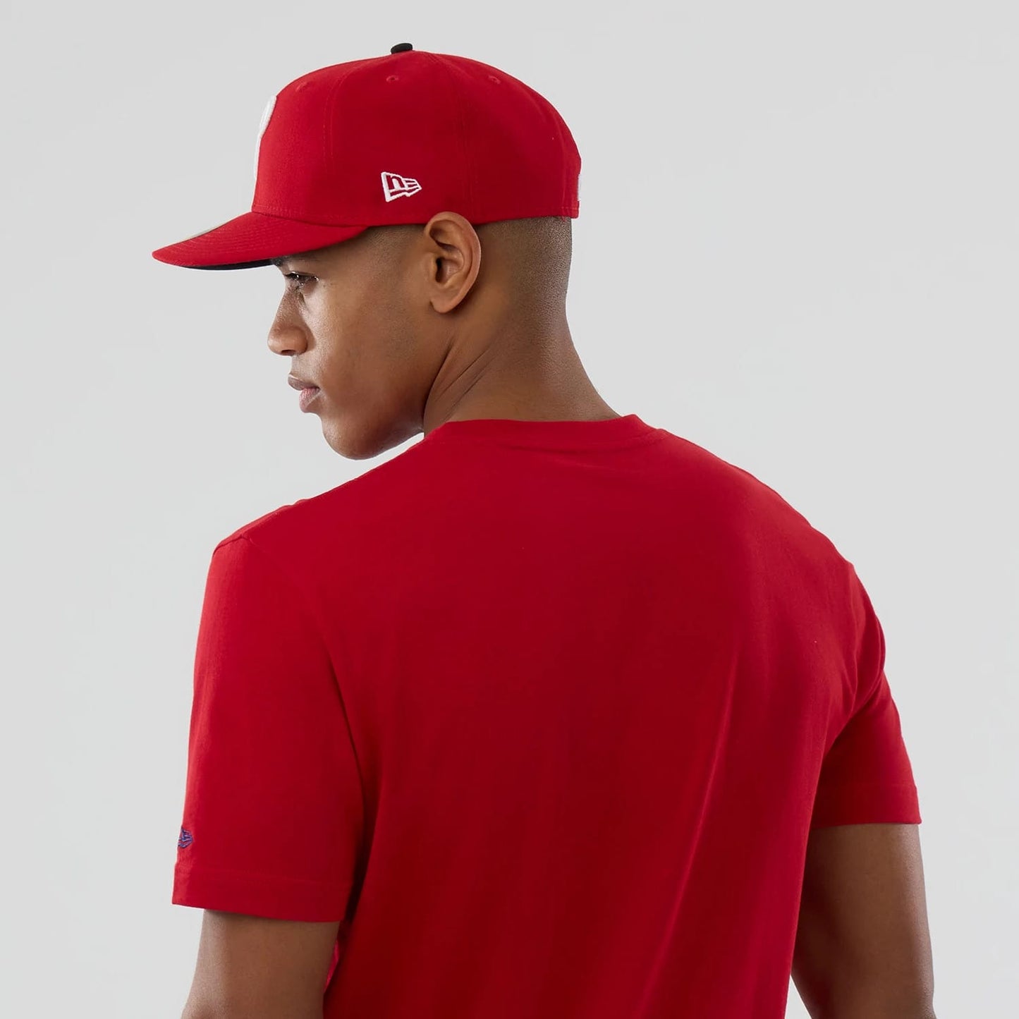 New Era Philadelphia Phillies MLB Popcorn Red T-Shirt, back view on a model styled with a matching red cap, showcasing the plain red back and the embroidered New Era logo on the left sleeve near the cuff.