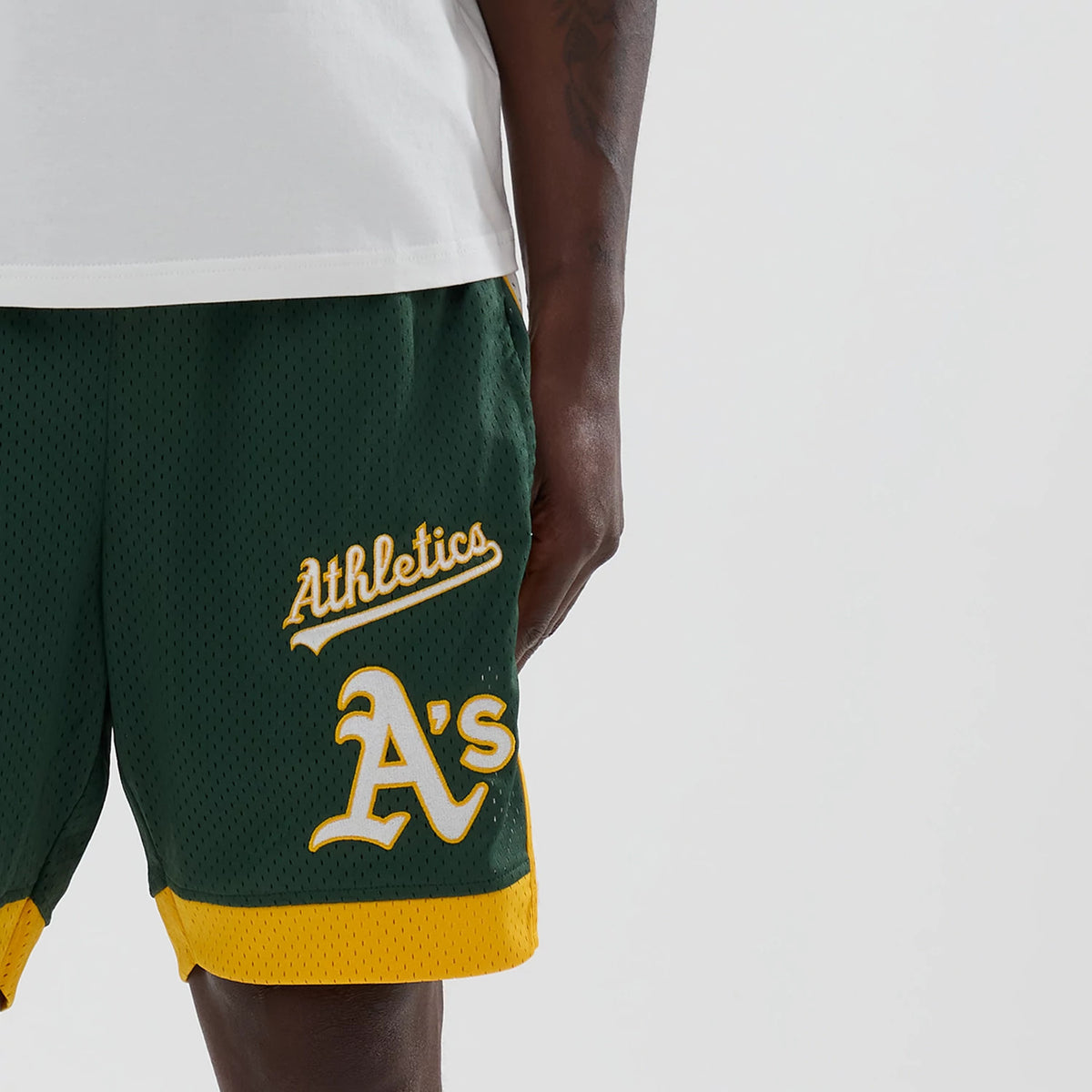 New Era Athletics MLB Dark Green Mesh Shorts, front view on-model showing yellow embroidered Athletics script and A's logo on a dark green background, with contrasting yellow trim at the hem.
