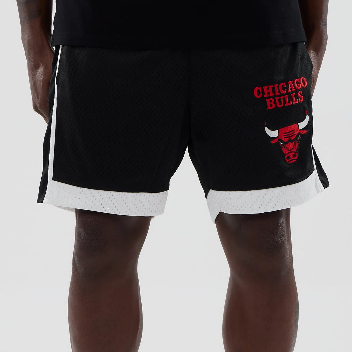 New Era Chicago Bulls NBA Black Mesh Shorts, front view on-model showing the red embroidered Chicago Bulls logo and lettering on the right leg, contrasting white trim on the hem, and black mesh fabric throughout.