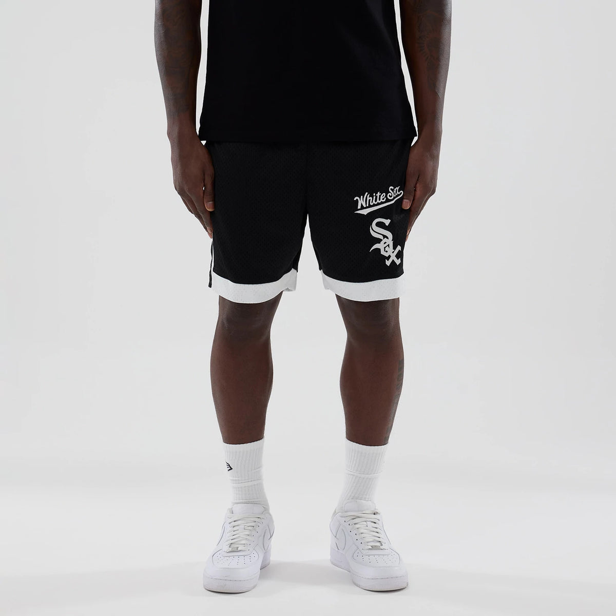 New Era Chicago White Sox MLB Black Mesh Shorts, front view on-model showing white embroidered White Sox script and logo on the left leg, contrasting white trim at the hem, paired with a black top and white trainers.
