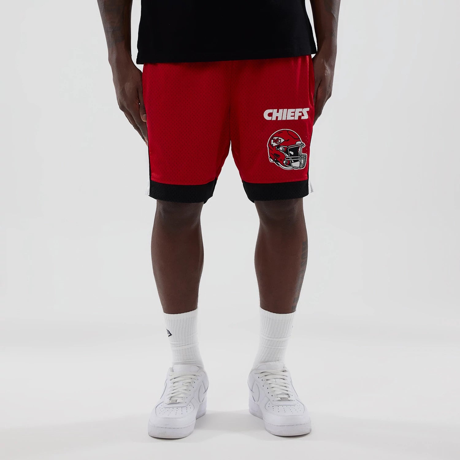 New Era Kansas City Chiefs NFL Red Mesh Shorts, front view on-model showing bright red shorts with white Chiefs lettering and a detailed printed helmet graphic on the left leg above a black banded hem.