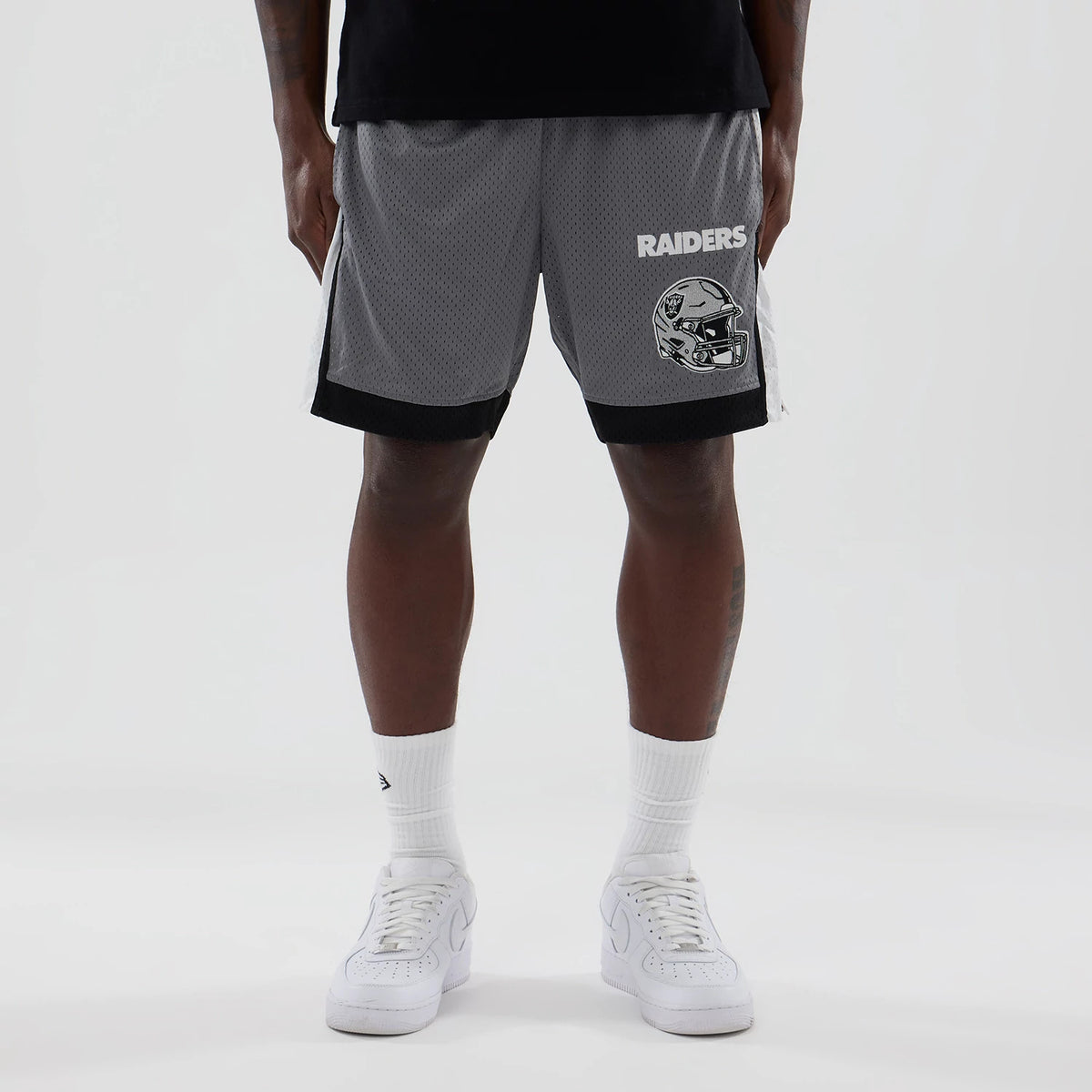 New Era Las Vegas Raiders NFL Grey Mesh Shorts, front view showing a black Raiders helmet graphic on the right leg, white Raiders text above, a black stripe at the bottom, and mesh across the grey fabric.