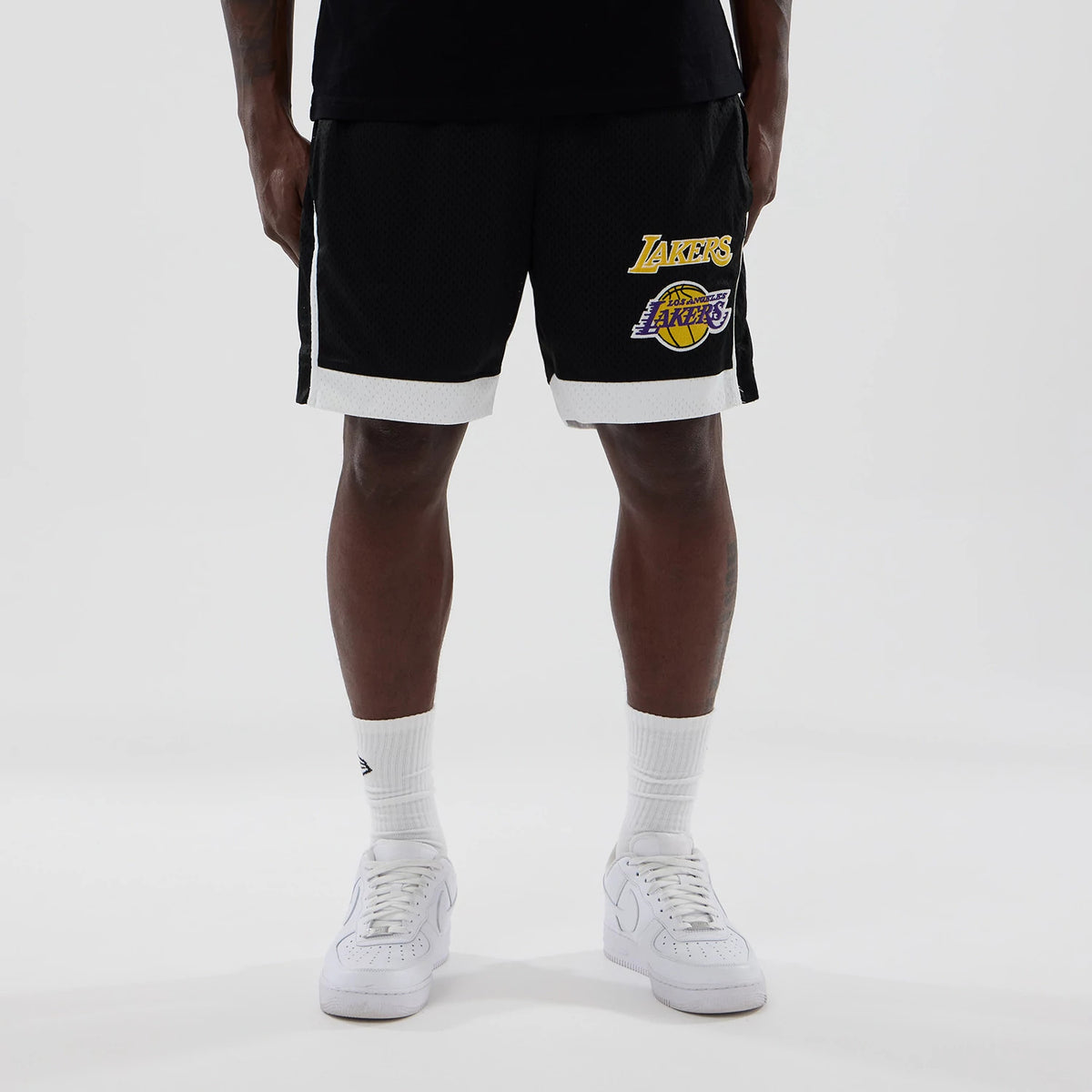 New Era LA Lakers NBA Black Mesh Shorts, front view on-model showing the gold embroidered Lakers logo on the left leg and the purple and gold team emblem below, with white trim at the hem and sides.