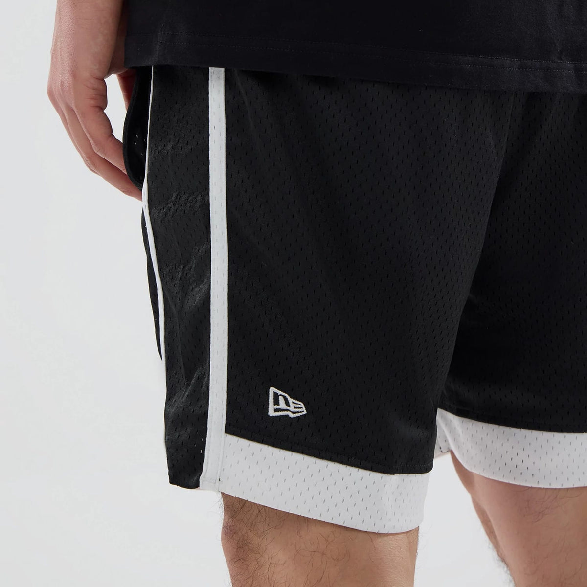 New Era LA Kings NHL Black Mesh Shorts, side view showing the black mesh fabric with white side stripes, a white embroidered New Era logo near the hem, and a white trim on the shorts' lower edge.