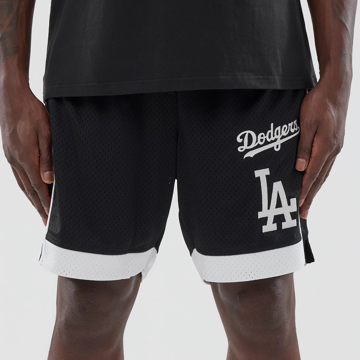 New Era LA Dodgers MLB Black Mesh Shorts, front view on a model showing a black mesh design with white embroidered Dodgers script high on the left leg and a large LA logo below, finished with white trim at the hem.