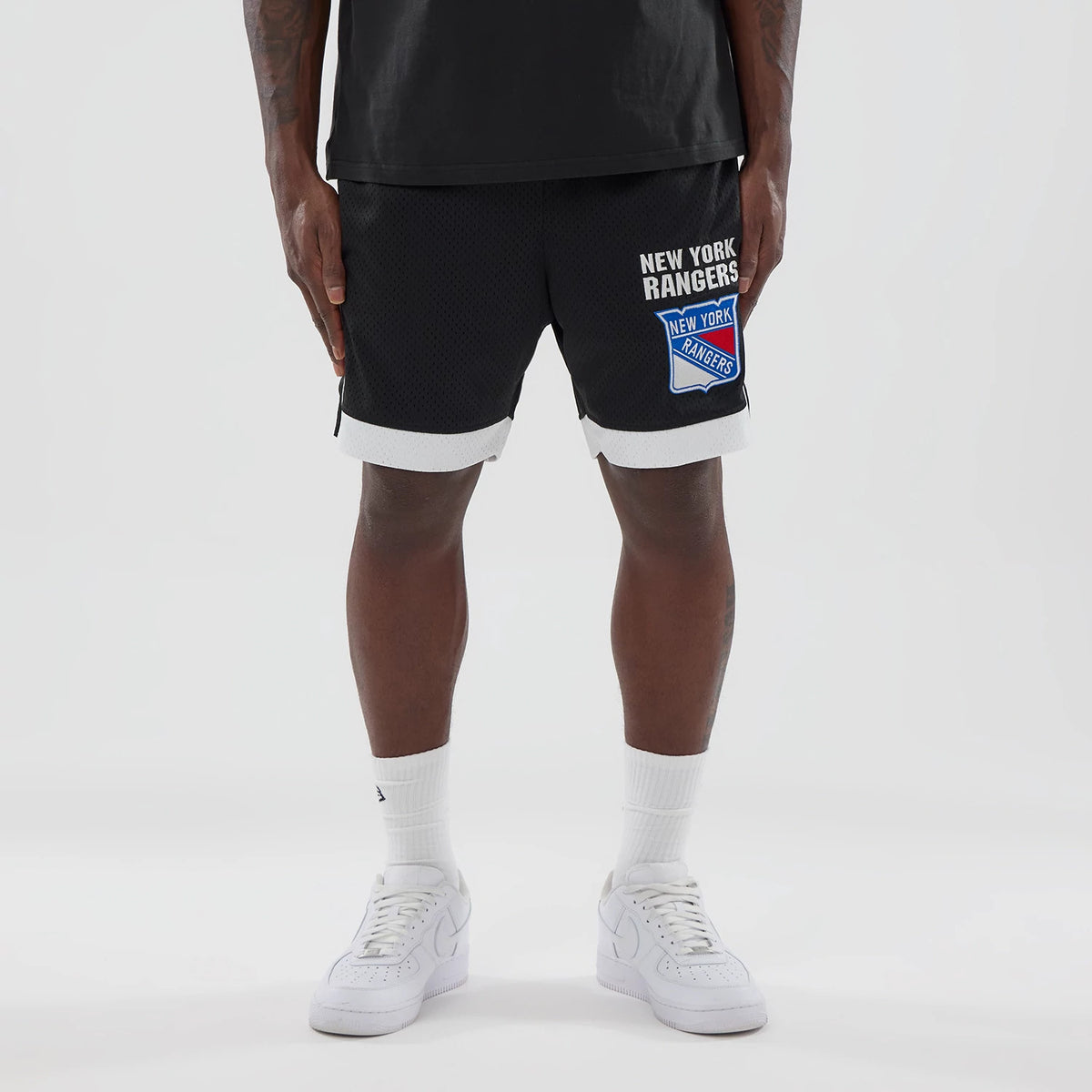 New Era New York Rangers NHL Black Mesh Shorts, front view on-model showing white printed New York Rangers lettering and a large team logo on the right leg, with contrasting white trim at the hem.