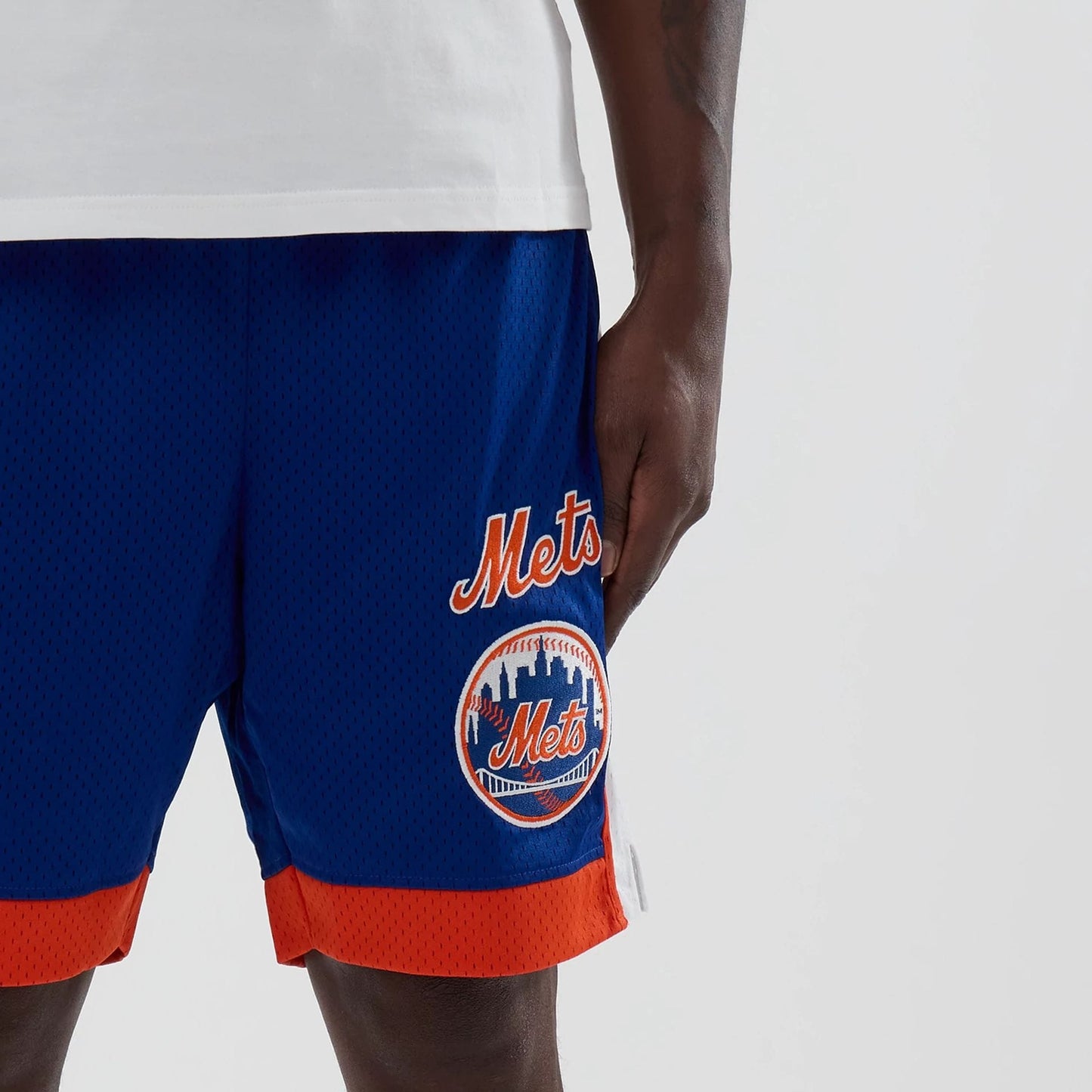 New Era New York Mets MLB Blue Mesh Shorts, three-quarter view showing the blue mesh fabric with an embroidered Mets logo and lettering on the left leg, finished with a contrasting orange trim along the edges.