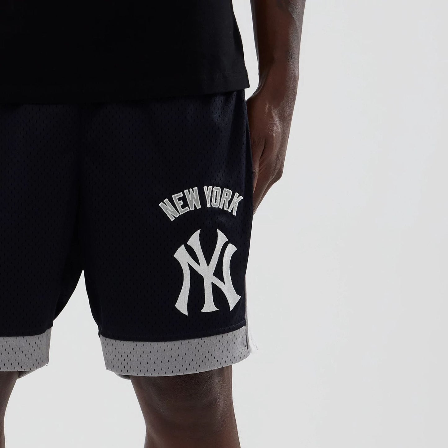 New Era New York Yankees MLB Navy Mesh Shorts, front view showing white embroidered New York Yankees logo and lettering on the left leg, dark navy mesh texture, and contrasting grey trim along the hem, styled with a black top on a model.
