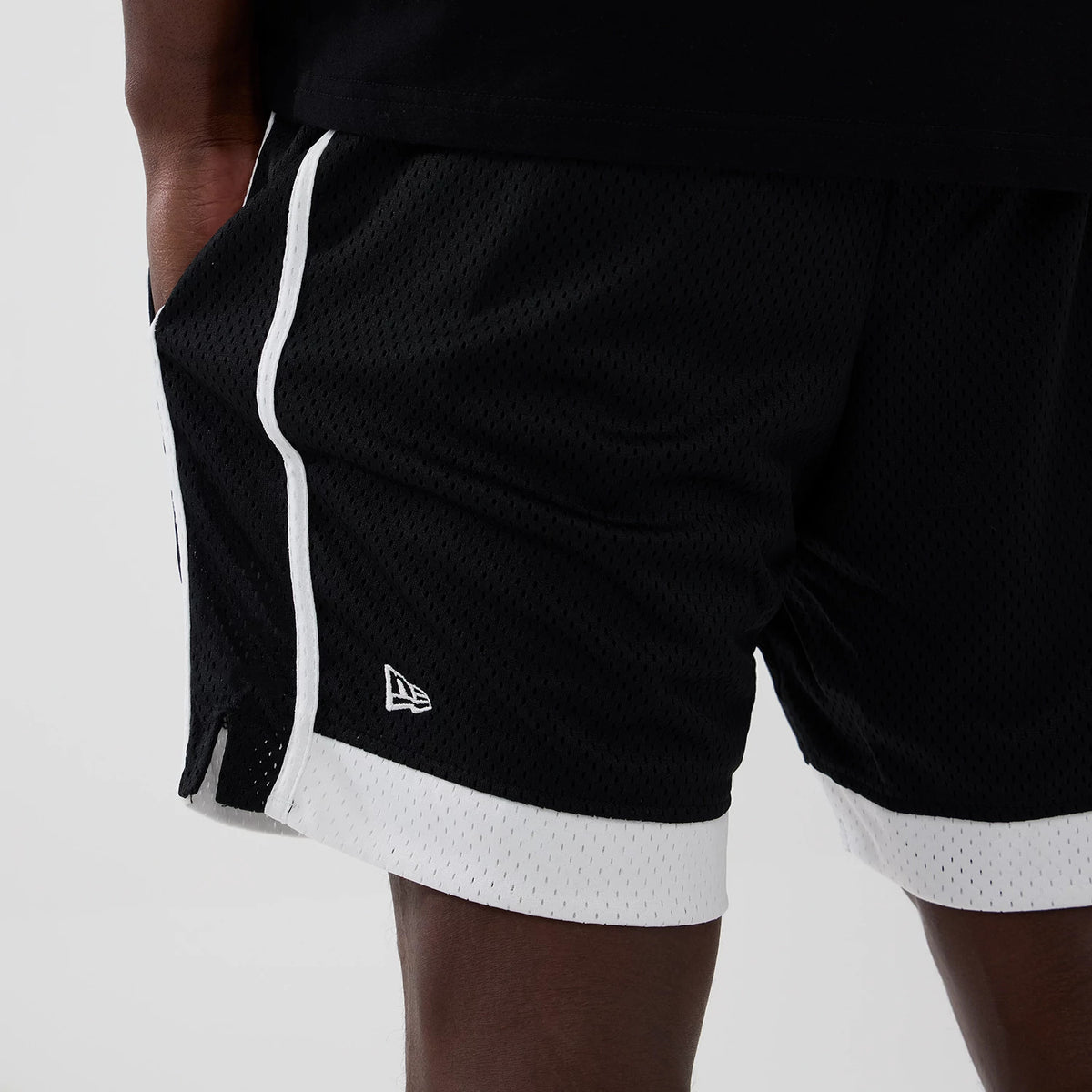 New Era New York Yankees MLB Black Mesh Shorts, three-quarter view showing black mesh fabric with white side stripes, a white embroidered New Era logo near the hem, and a white trim on the hem for a contrast.