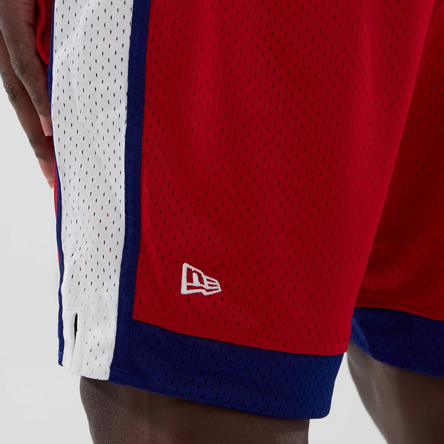 New Era Philadelphia Phillies MLB Red Mesh Shorts, side view showing the red mesh fabric with a vertical white and blue stripe, an embroidered New Era logo in white near the hem contrasting against the red material.