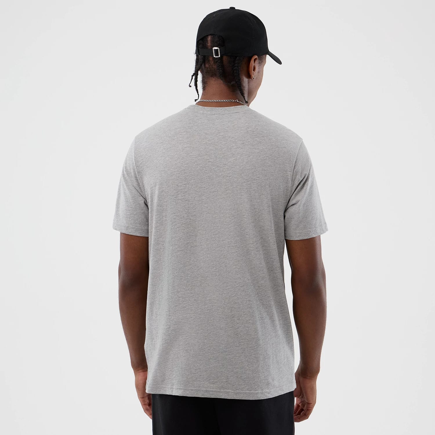 New Era Back To School Grey T-Shirt, back view on a model, highlighting the plain grey fabric with a simple round neck and short sleeves, styled casually with a black cap and dark trousers.