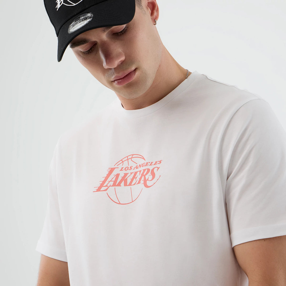 New Era LA Lakers NBA Back To School Graphic White T-Shirt, front view on a model paired with a black cap, featuring a pink printed Los Angeles Lakers logo across the chest with lettering over a basketball graphic.