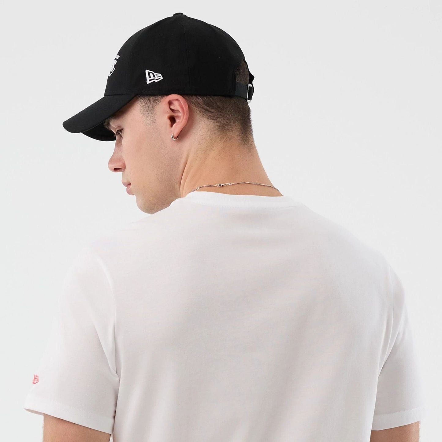 New Era LA Lakers NBA Back To School Graphic White T-Shirt, back view on-model showing a plain white back and short sleeves, paired with a black cap featuring an embroidered New Era logo on the side.