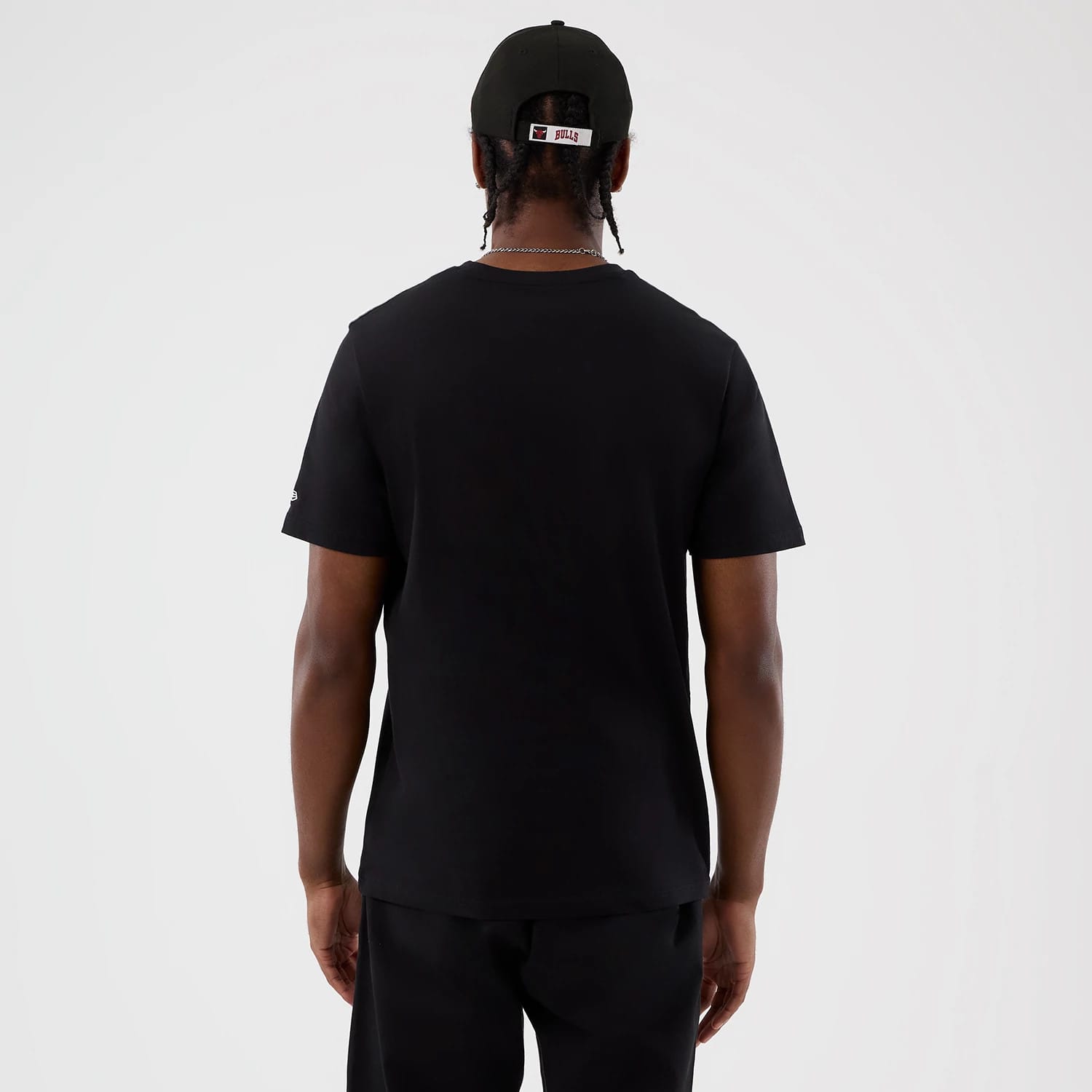 New Era Chicago Bulls NBA Back To School Black T-Shirt, back view on a model wearing a matching black cap, showing a plain back with short sleeves and an embroidered New Era logo on the left sleeve.