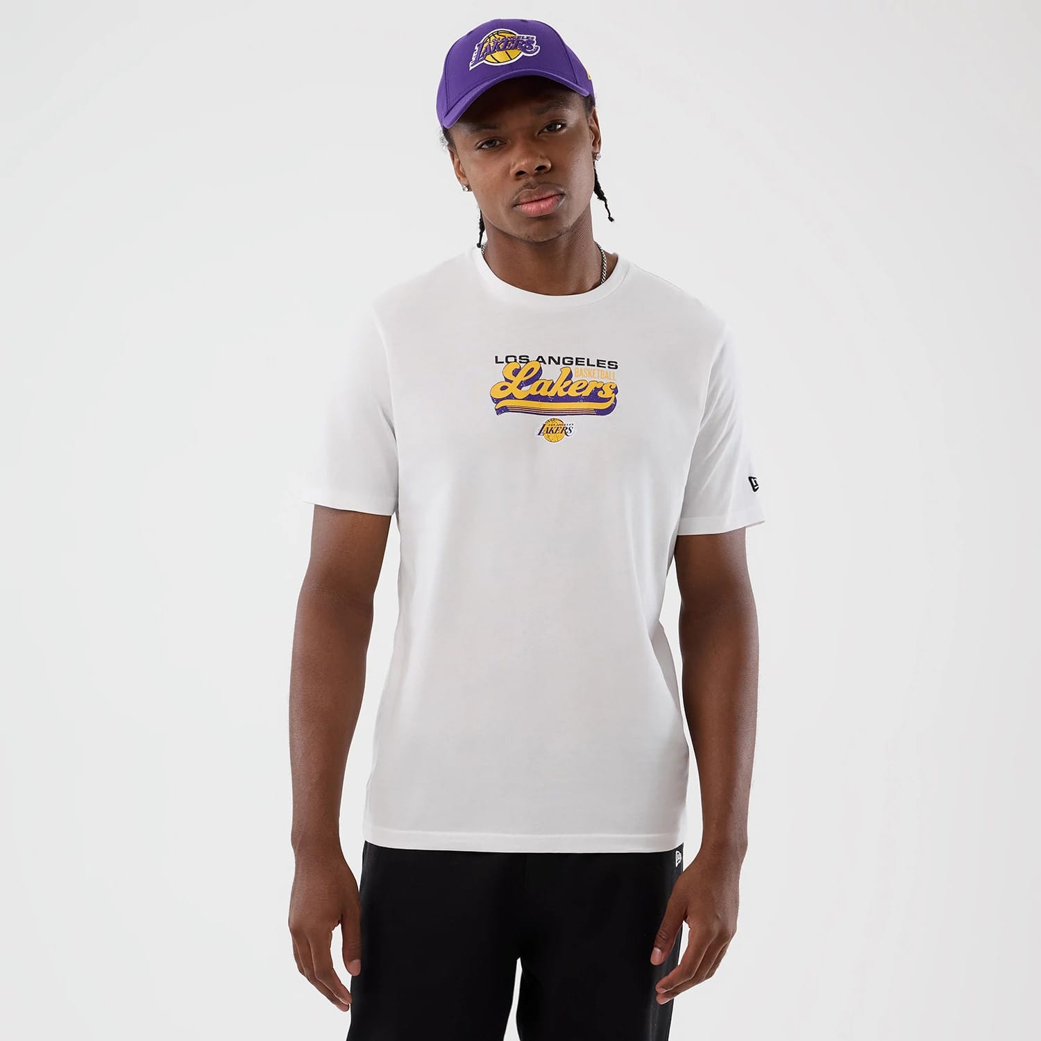 New Era LA Lakers NBA Script Back To School White T-Shirt, front view on-model showing embroidered Lakers graphic across the chest in yellow and purple, small New Era logo on the sleeve, styled with a purple cap.