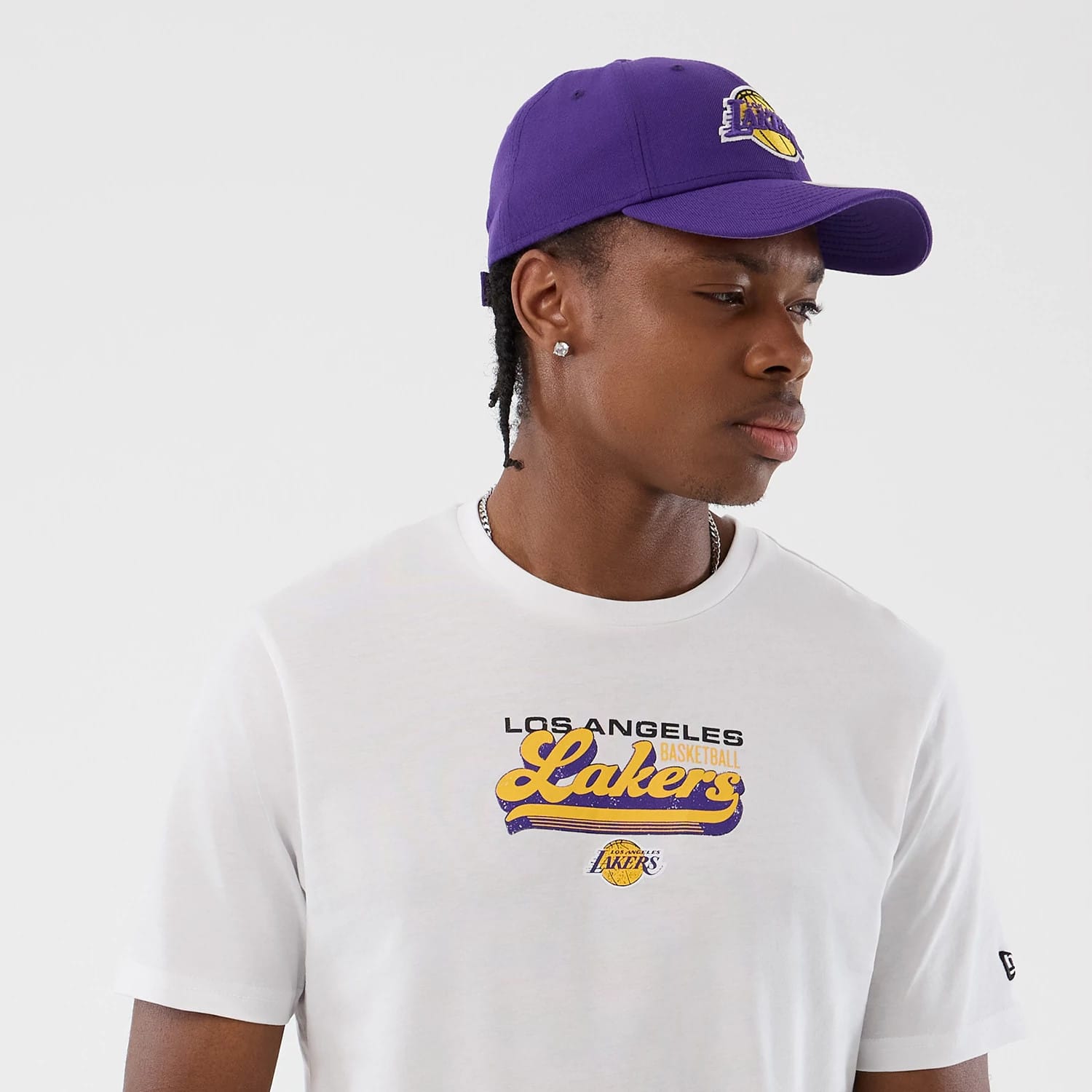New Era LA Lakers NBA Script Back To School White T-Shirt, front view on-model showing the Lakers script logo embroidered in yellow and purple across the chest, paired with a purple cap featuring the team's emblem on the front.