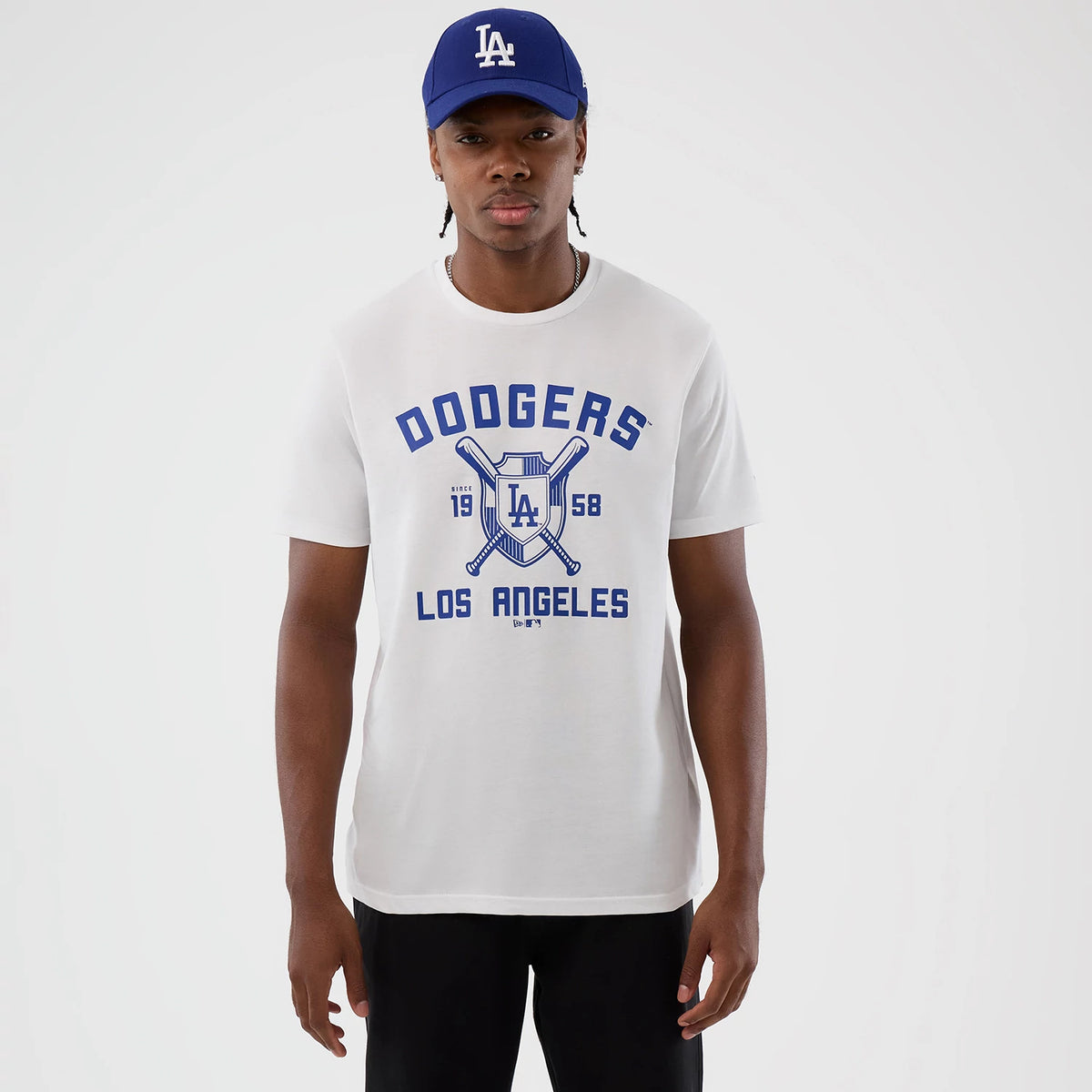 New Era LA Dodgers MLB Back To School White T-Shirt, front view on-model showing a large blue Dodgers graphic with bats and LA logo centred on the chest, blue LOS ANGELES lettering below, paired with a blue cap.