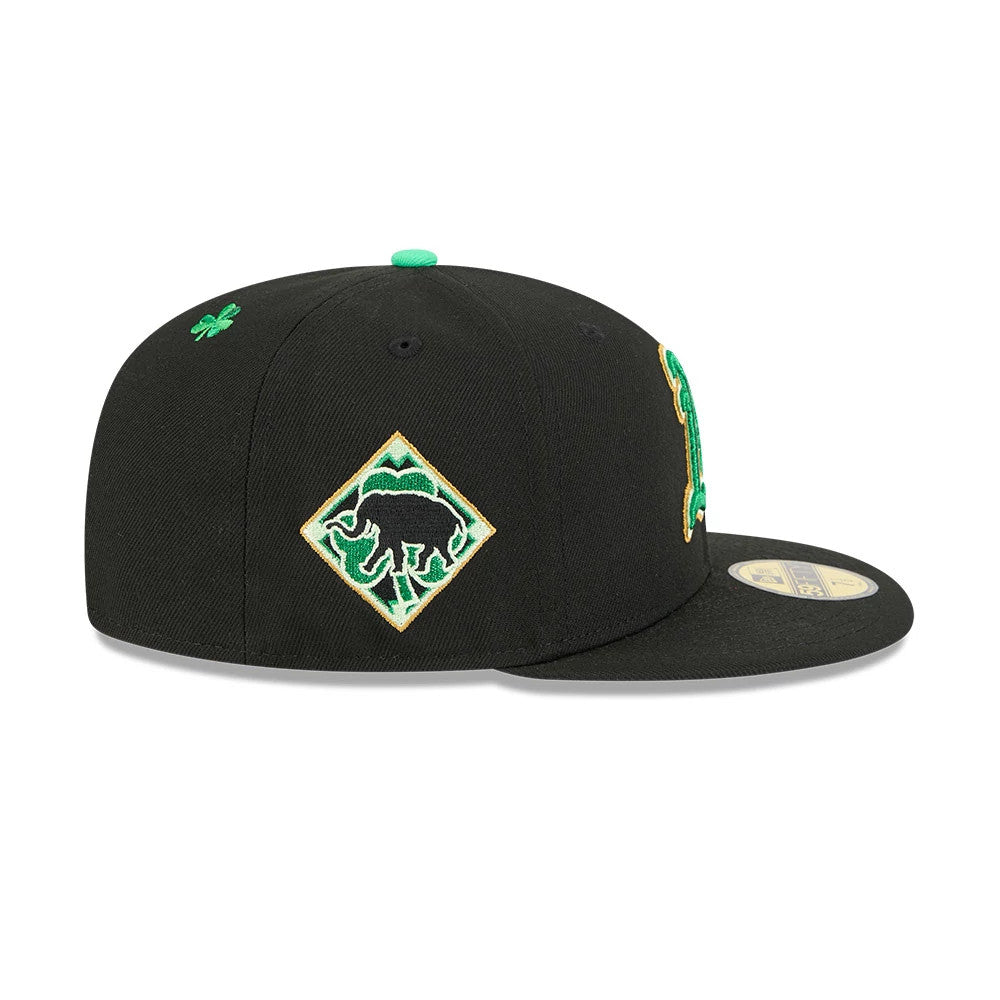 Athletics MLB Saint Patrick's Day Black New Era 59FIFTY Fitted Cap, side view showing the green and gold embroidered elephant patch on the side panel, with a small green clover on the top and a gold 59FIFTY size sticker on the flat visor.