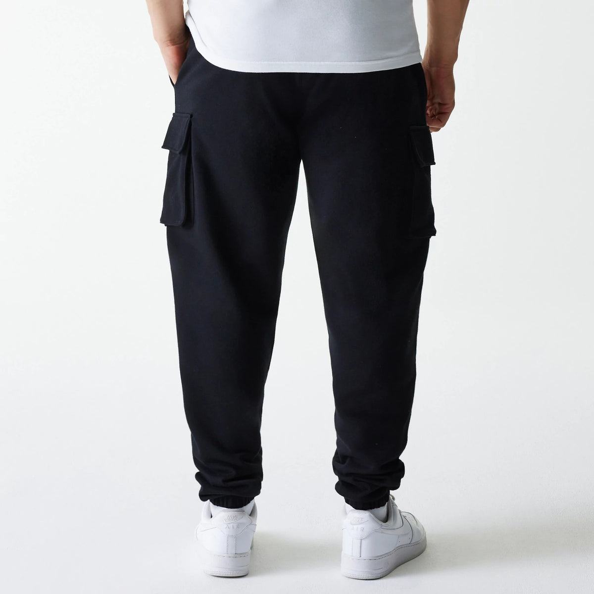 New Era Black Cargo Joggers, rear view showing multiple large pockets on the side of each leg, elasticated cuffs at the ankles, and side seam pockets, crafted from a comfortable black fabric.