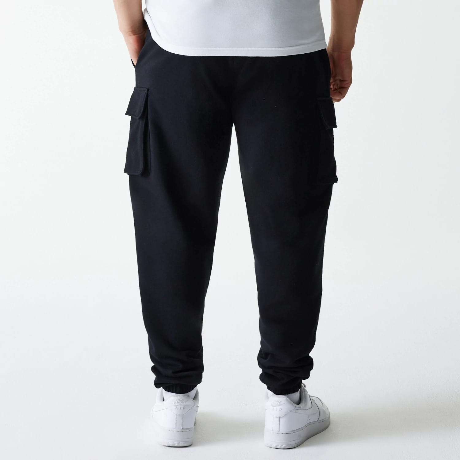 New Era Black Cargo Joggers, rear view showing multiple large pockets on the side of each leg, elasticated cuffs at the ankles, and side seam pockets, crafted from a comfortable black fabric.