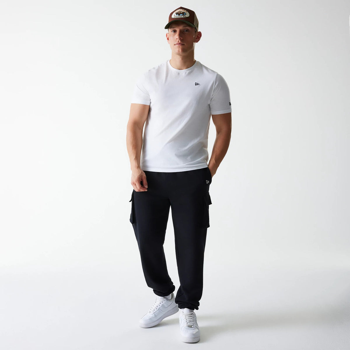New Era Black Cargo Joggers, on-model view showing the joggers' relaxed fit and side cargo pockets, styled with a white T-shirt and white sneakers, highlighting the small New Era flag logo on the upper left leg.
