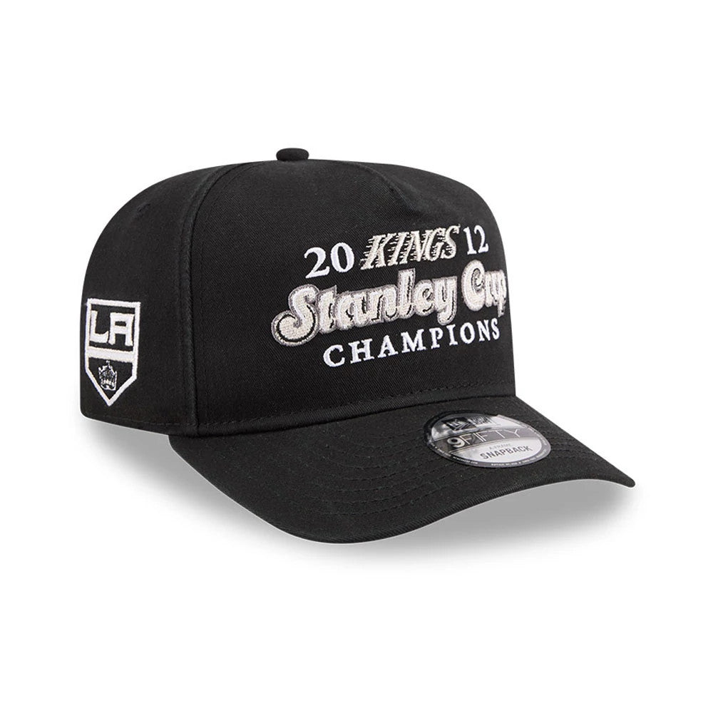 LA Kings NHL Historic Black New Era 9FIFTY A-Frame Snapback Adjustable Cap, front view showing grey embroidered Stanley Cup Champions lettering across the front panels and LA logo on the left side, with a black visor and 9FIFTY size sticker.